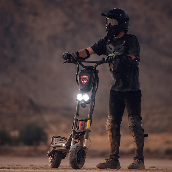 Rider standing with Kaabo Warrior 11 Pro+ electric scooter in desert terrain wearing full protective gear